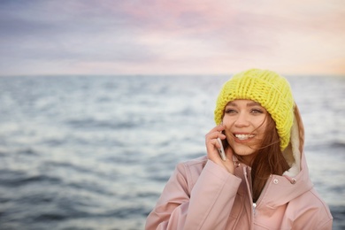 Photo of Young woman talking on mobile phone near sea