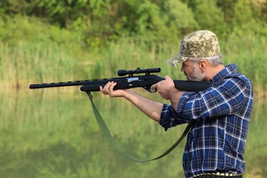 Photo of Man aiming with hunting rifle near lake outdoors