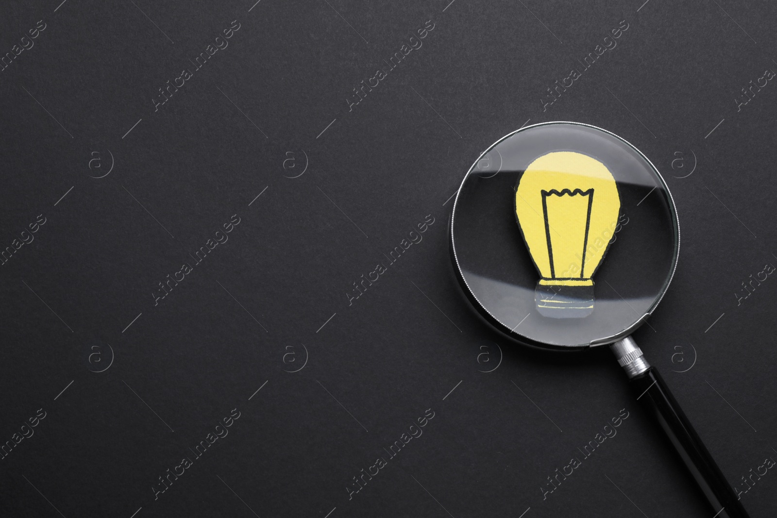Photo of Magnifying glass over paper light bulb on dark background, top view. Space for text