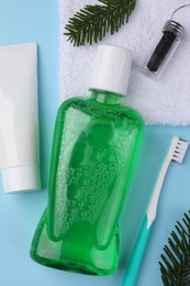 Fresh mouthwash in bottle, toothbrush, toothpaste and dental floss on light blue background, flat lay