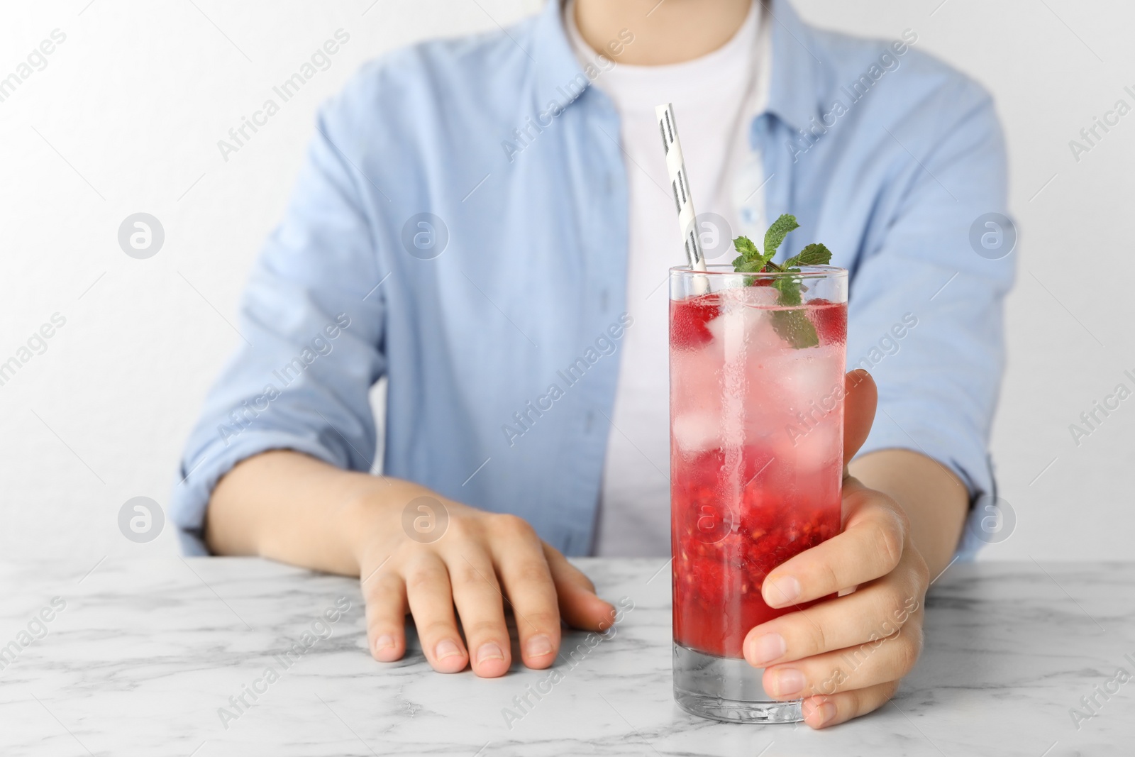 Photo of Woman with glass of raspberry refreshing drink at marble table, closeup