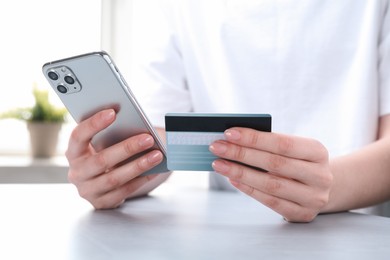 Photo of Online payment. Woman with smartphone and credit card at white table, closeup