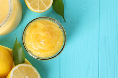 Delicious lemon curd in jar, fresh citrus fruits and green leaves on light blue wooden table, flat lay. Space for text