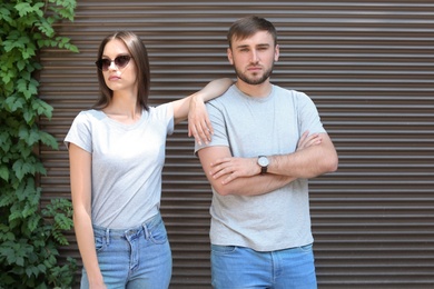Photo of Young couple wearing gray t-shirts near wall on street.