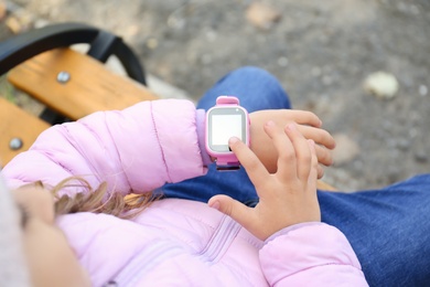 Photo of Little girl using smart watch on bench outdoors, closeup