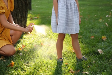 Photo of Mother applying insect repellent onto girl's leg in park, closeup