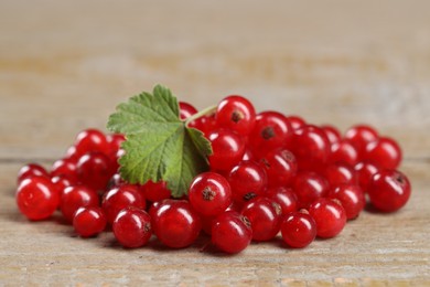 Photo of Pile of ripe red currants and leaf on wooden table, closeup