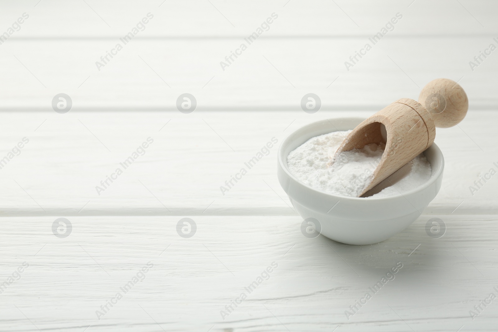 Photo of Baking powder in bowl and scoop on white wooden table, space for text