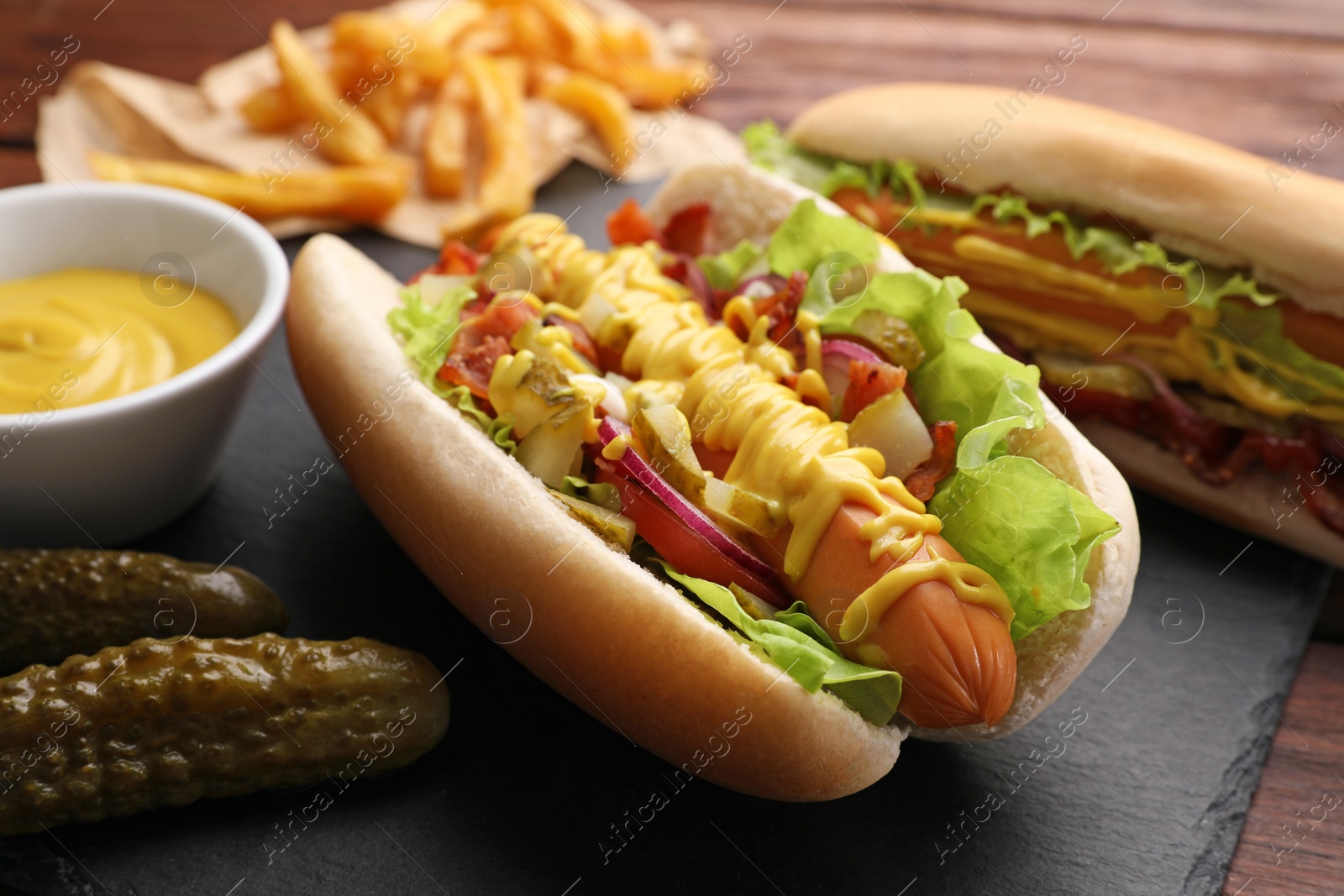 Photo of Delicious hot dogs with lettuce, onion and pickle served on table, closeup