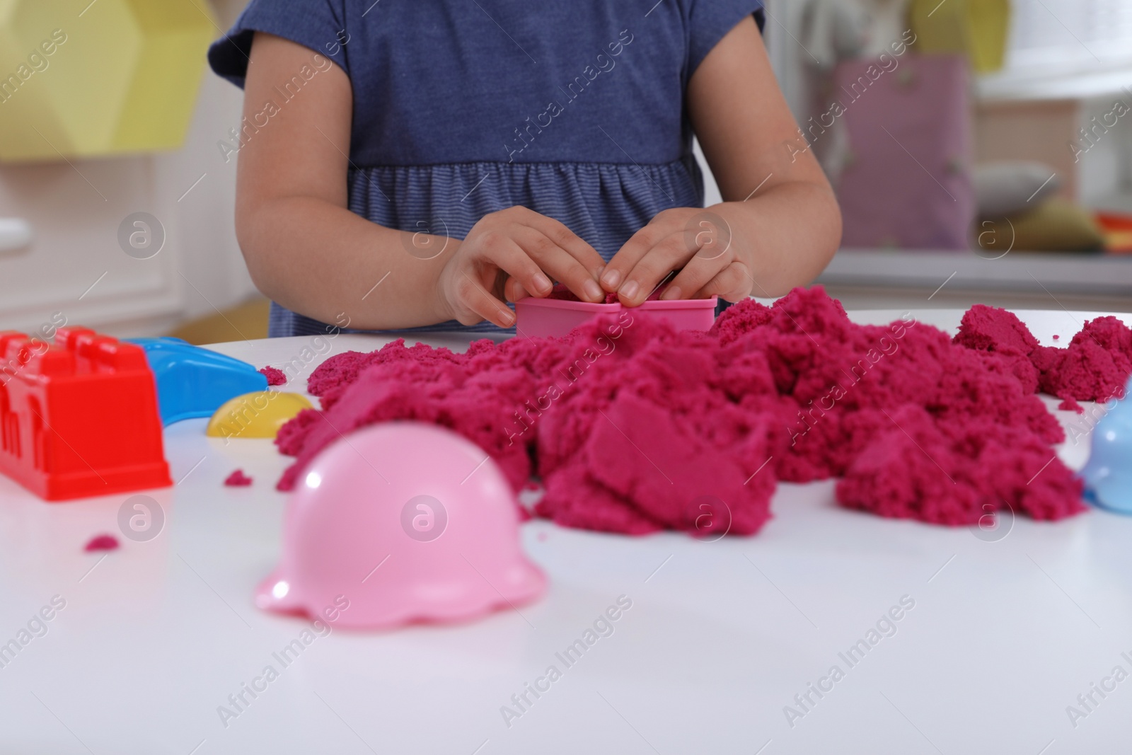 Photo of Little girl playing with bright kinetic sand at table indoors, closeup