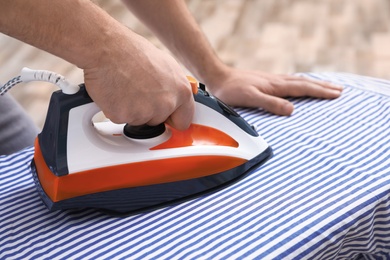 Photo of Man ironing shirt on board at home, closeup