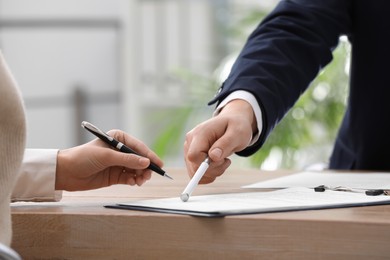 Businesspeople signing contract at table in office, closeup