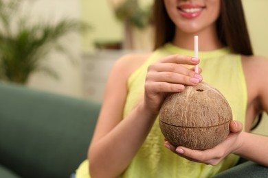 Young woman with fresh coconut at home, closeup. Exotic fruit