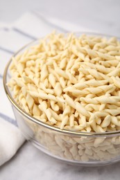 Uncooked trofie pasta in bowl on white table, closeup