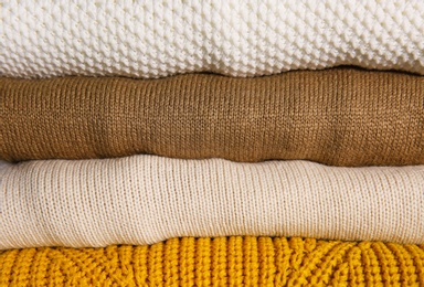 Stack of folded knitted sweaters as background, closeup