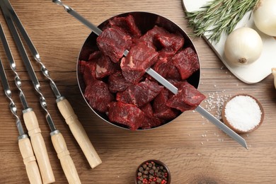 Photo of Flat lay composition with metal skewers and bowl of raw meat on wooden table