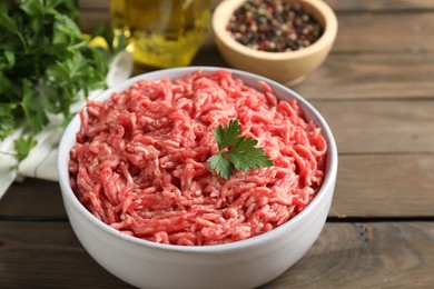 Photo of Raw ground meat in bowl, parsley, spices and oil on wooden table, closeup