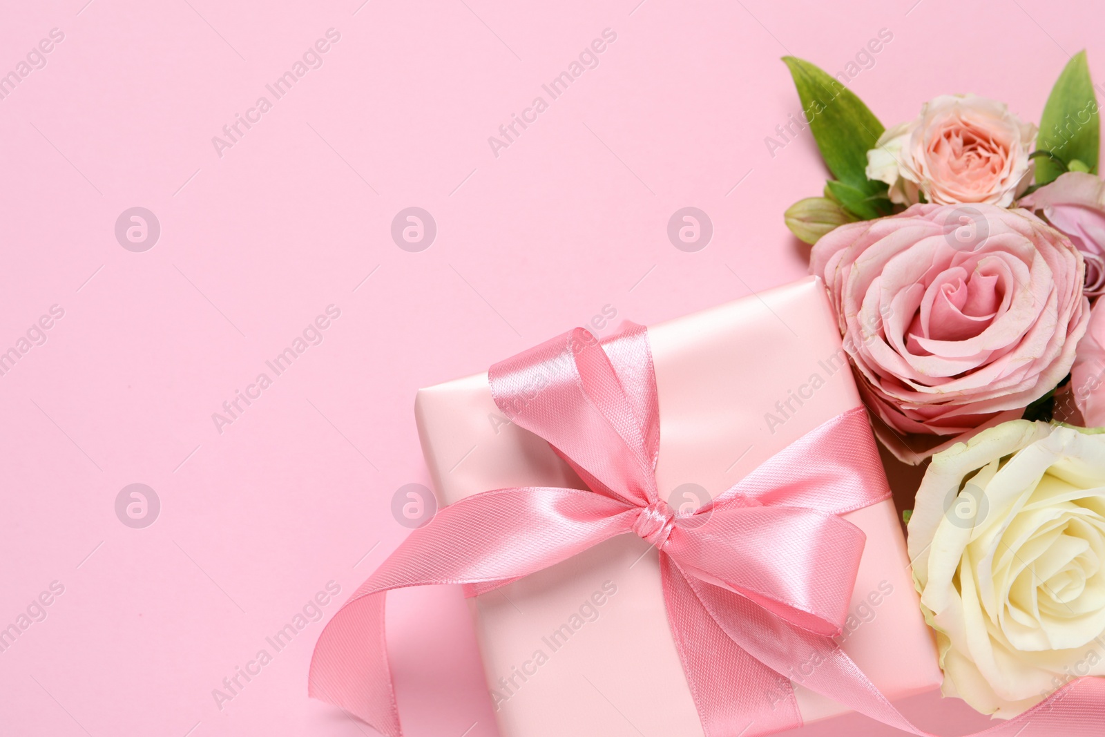 Photo of Gift box and beautiful flowers on pink background, flat lay. Space for text