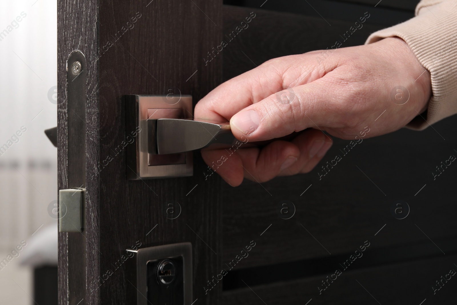 Photo of Man opening wooden door indoors, closeup of hand on handle