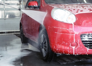 Cleaning modern automobile with high pressure water jet at car wash
