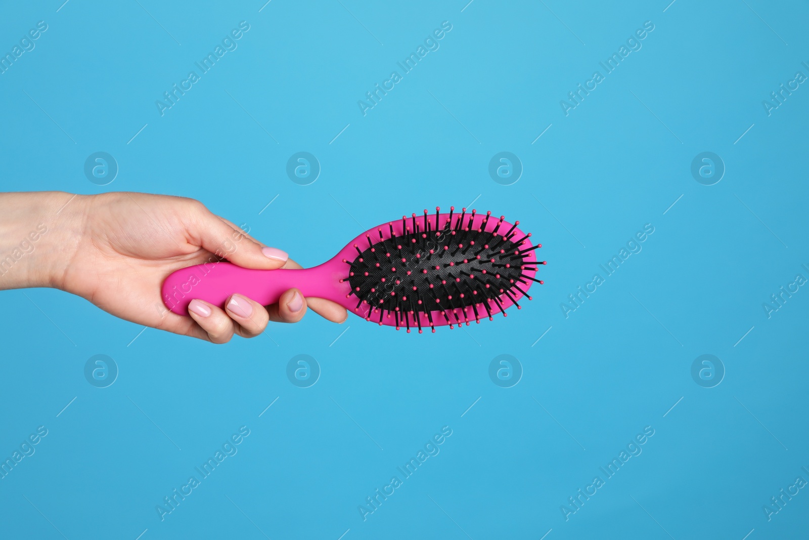 Photo of Woman holding hair brush against blue background, closeup