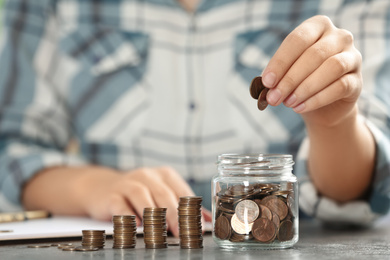 Woman putting money into glass jar at table, closeup