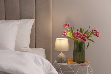 Photo of Stylish lamp, flowers and magazine on bedside table indoors. Bedroom interior elements