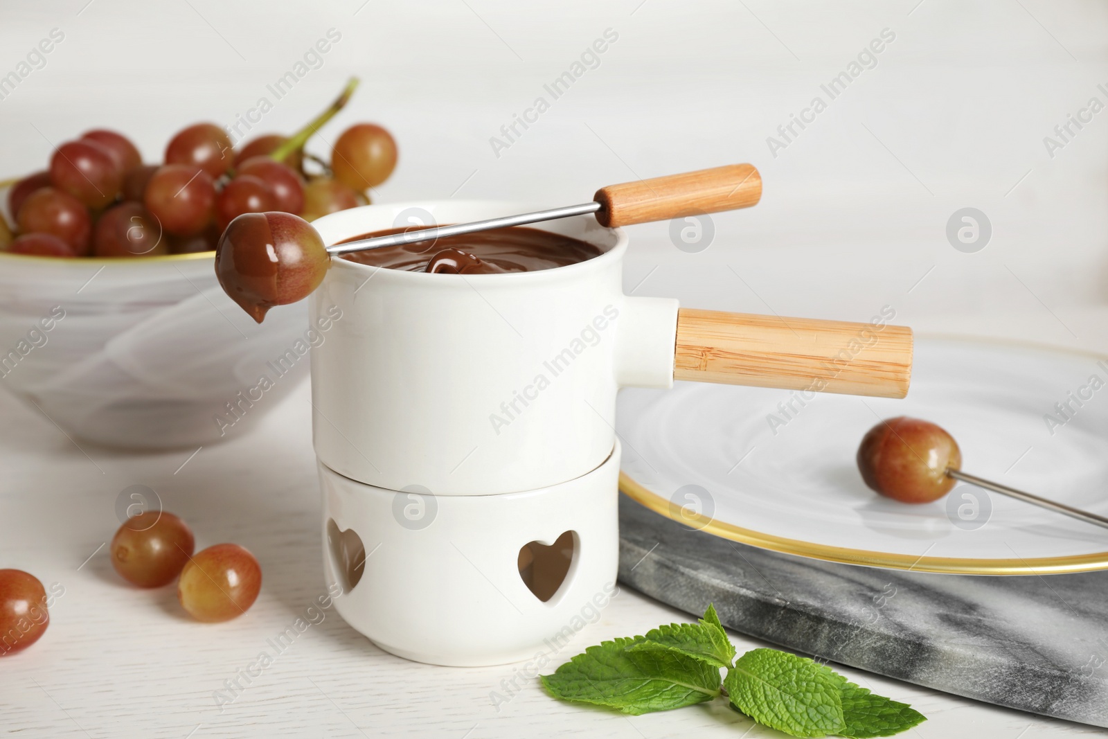 Photo of Fondue pot with chocolate and grape on white wooden table