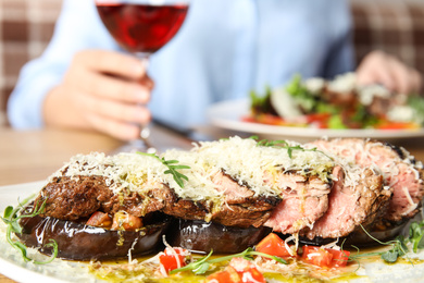 Photo of Delicious roasted meat and blurred woman on background, closeup