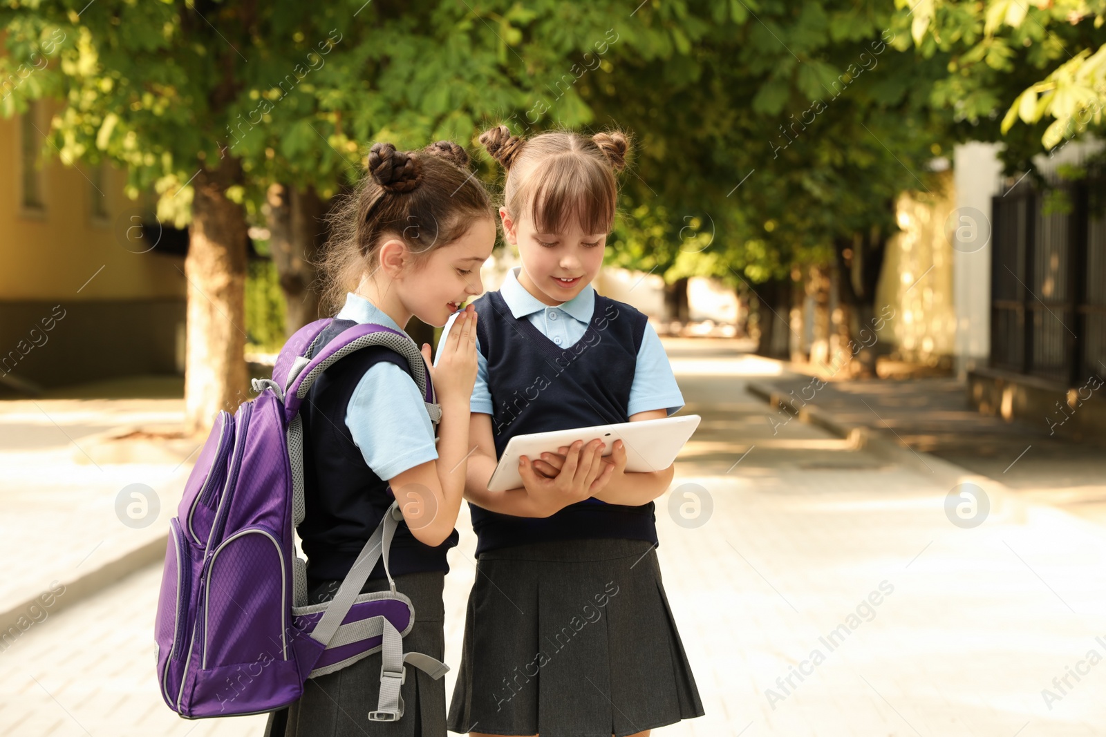 Photo of Little girls in stylish school uniform with tablet outdoors