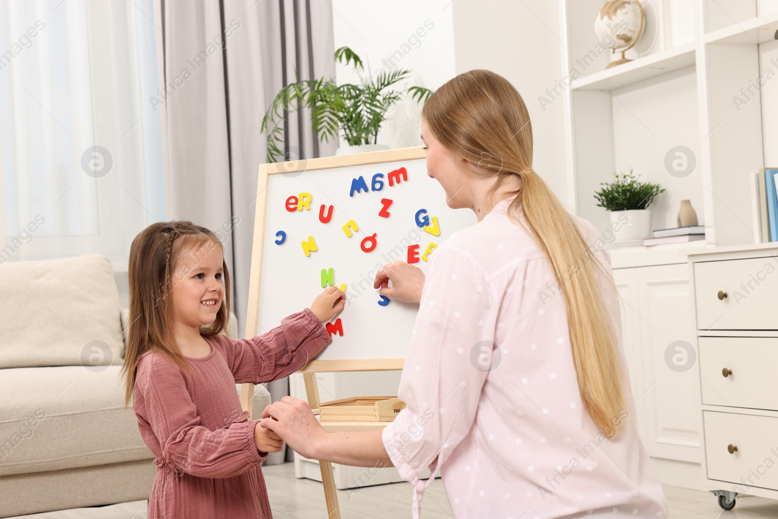 Photo of Mom teaching her daughter alphabet with magnetic letters at home