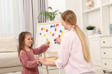 Mom teaching her daughter alphabet with magnetic letters at home