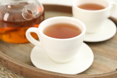 Photo of Aromatic tea in cups and teapot on wooden tray, closeup