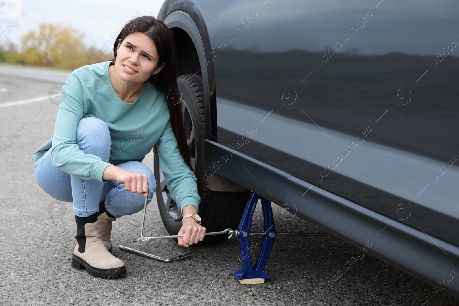 Photo of Young woman changing tire of car on roadside