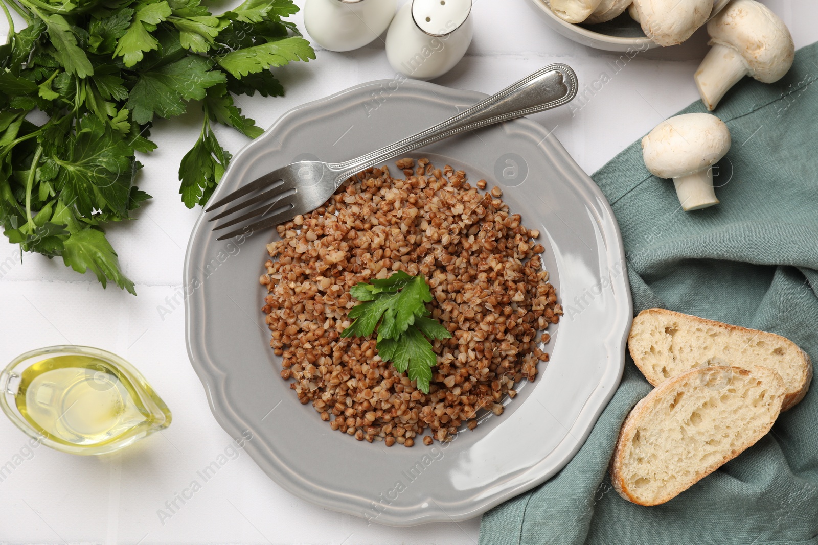 Photo of Tasty buckwheat with parsley served on white tiled table, flat lay