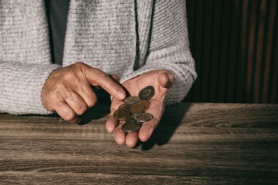 Photo of Poor senior woman with coins at table, closeup. Space for text