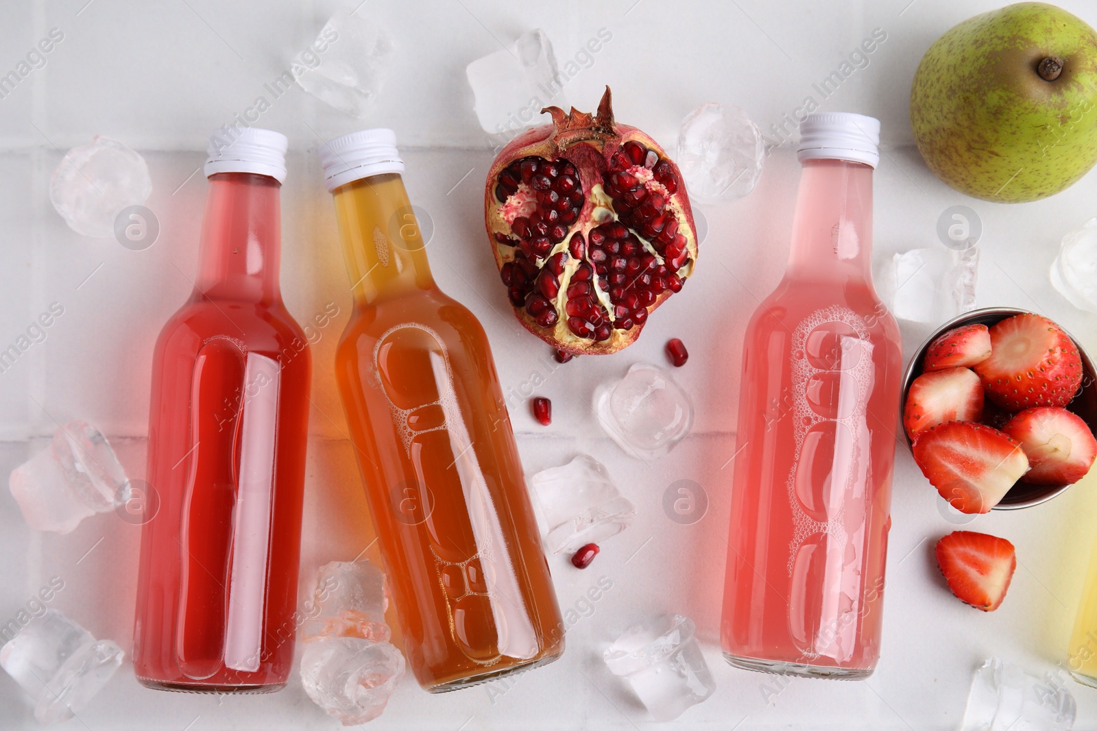 Photo of Tasty kombucha in glass bottles, fresh fruits and ice on white table, flat lay