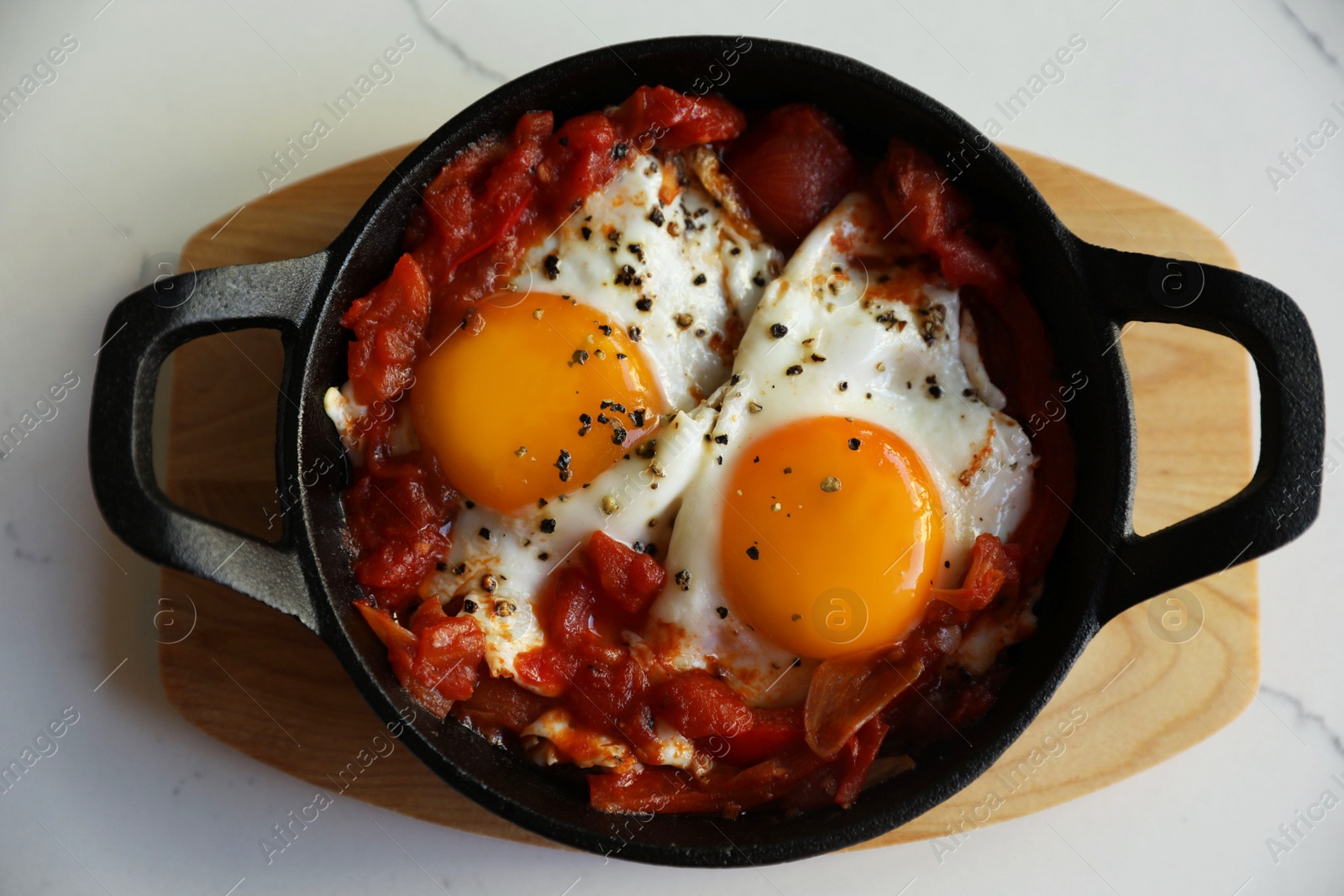 Photo of Tasty Shakshouka served in pan on white marble table, top view