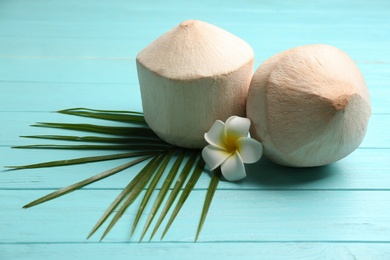 Photo of Young peeled coconuts with palm leaf and flower on light blue wooden table