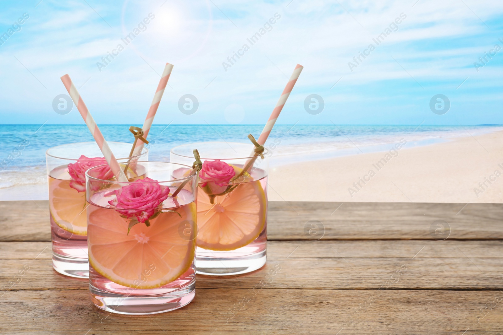 Image of Tasty refreshing drink on wooden table against sandy beach