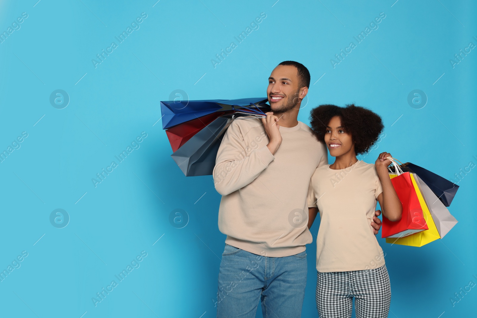 Photo of Happy African American couple with shopping bags on light blue background. Space for text