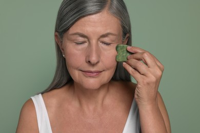 Photo of Woman massaging her face with jade gua sha tool on green background
