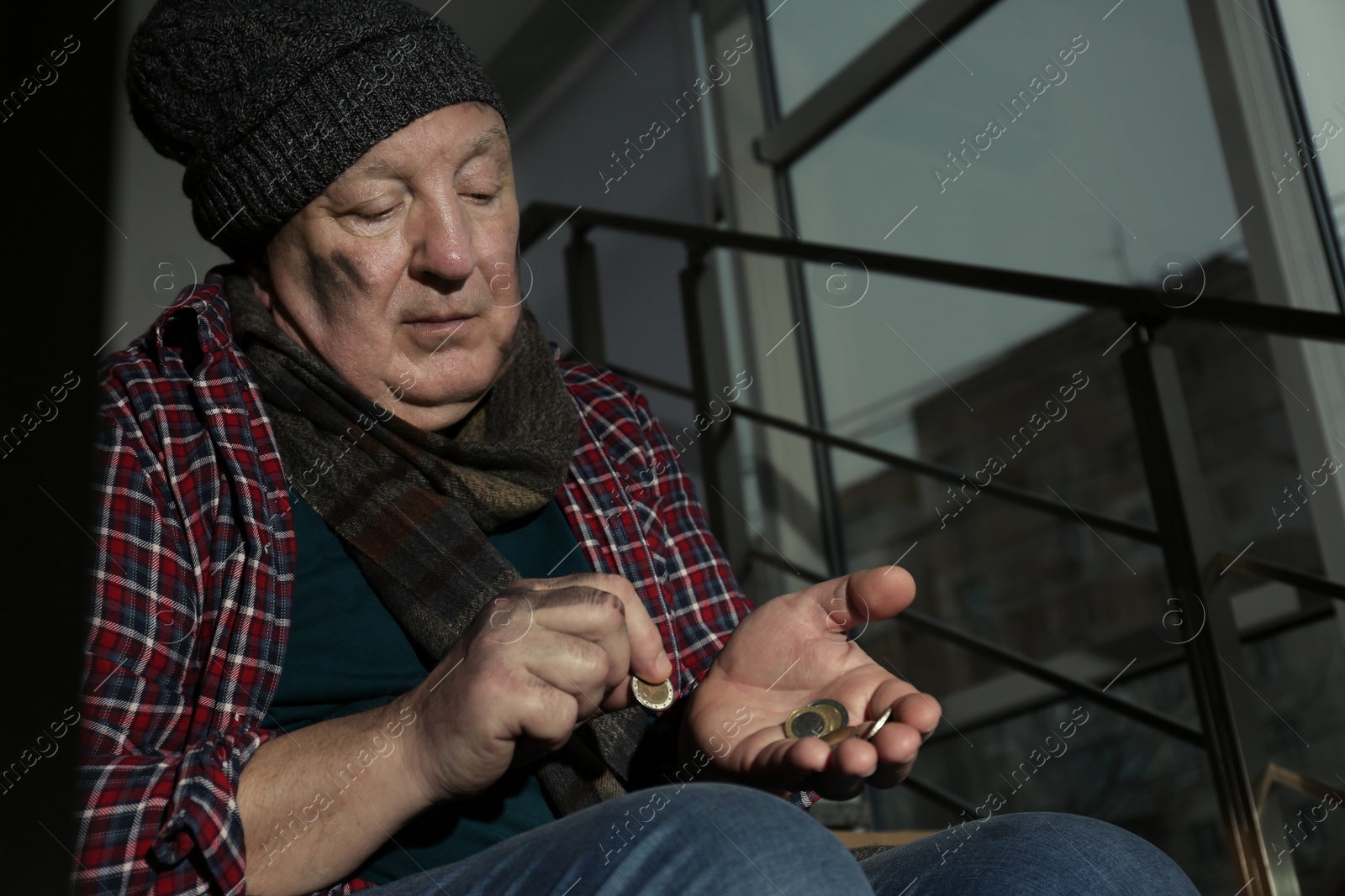 Photo of Poor senior man counting coins on stairs indoors. Space for text