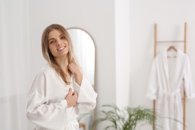 Beautiful happy woman wearing stylish white robe in bathroom. Space for text