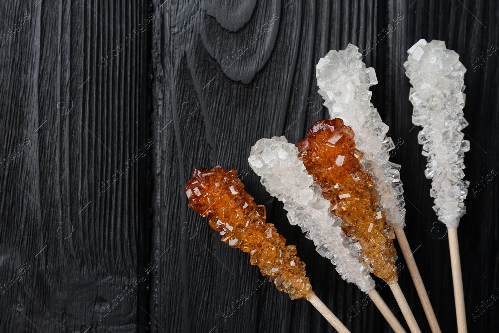 Photo of Sticks with sugar crystals on black wooden table, flat lay and space for text. Tasty rock candies