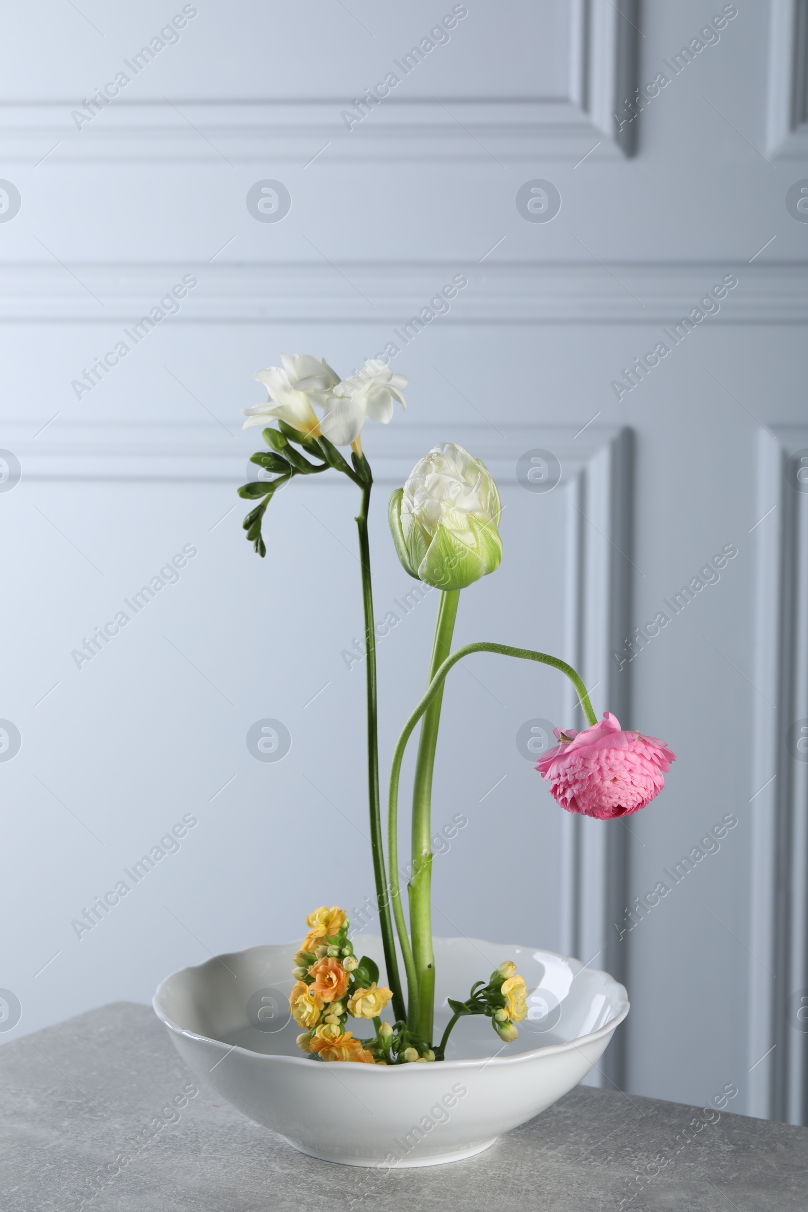 Photo of Stylish ikebana as house decor. Beautiful fresh flowers on grey table near white wall