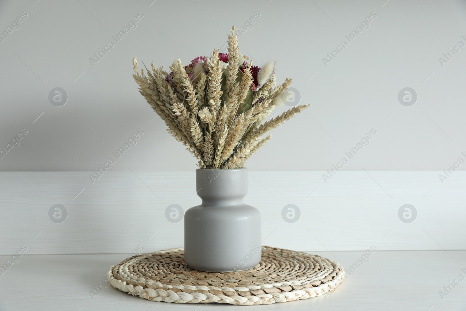 Photo of Beautiful bouquet of dry flowers on table near light wall