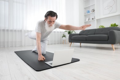 Senior man in sportswear exercising while watching online tutorial at home
