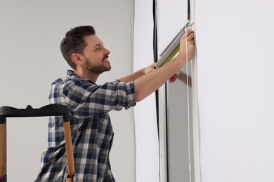 Photo of Man measuring window with tape on stepladder indoors. Roller blinds installation