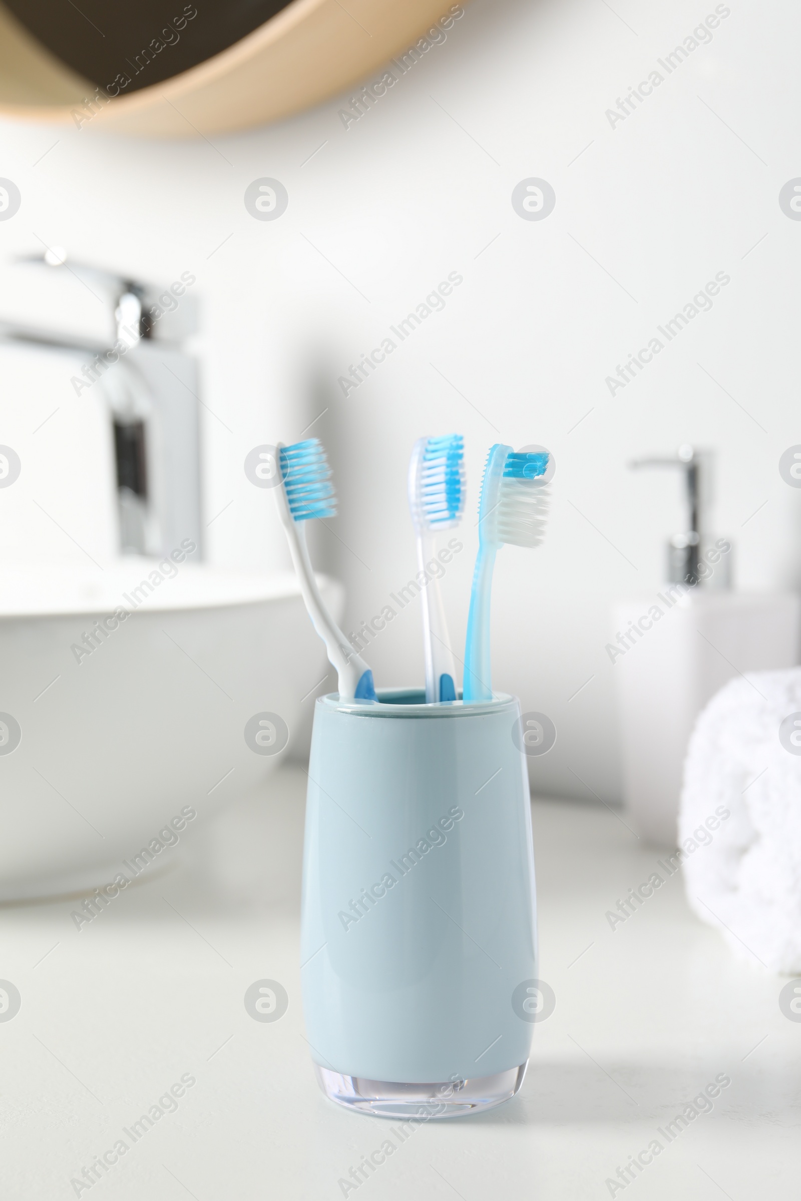 Photo of Holder with plastic toothbrushes on white countertop in bathroom